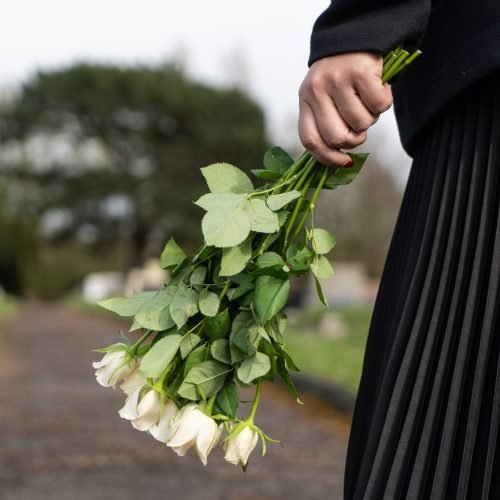 woman dressed in black carrying white rose bouquet at funeral